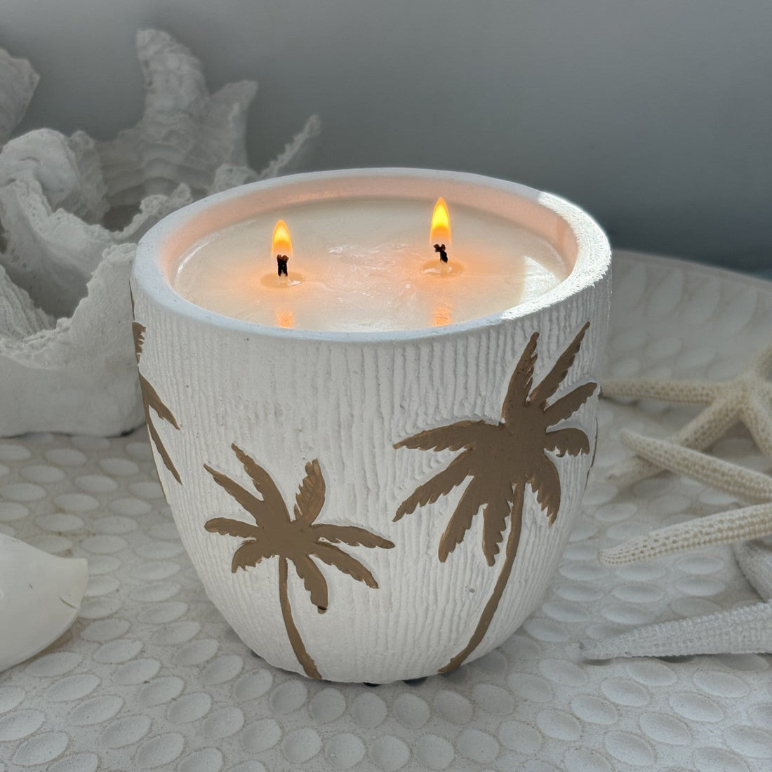 Candle in a decorative holder with palm tree designs on a textured surface.